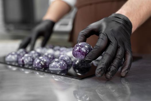 Close-up of the hand of a male pastry chef-a man laying out colored chocolates on a black mirror surface.