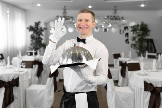Portrait of a young male waiter in a uniform showing the ok sign.