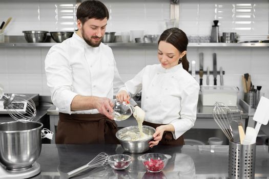 Pastry chef a man and a woman in a professional kitchen prepare a sponge cake, mix the ingredients. Joint work of a married couple.