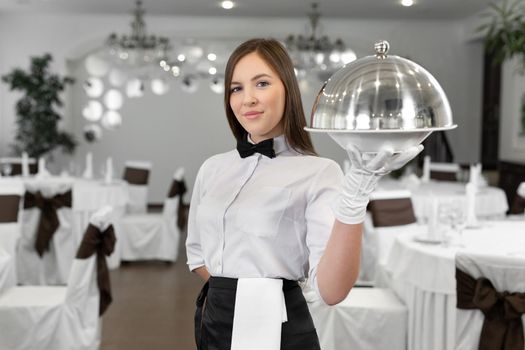 Female waiter holds a closed tray with a hot dish.