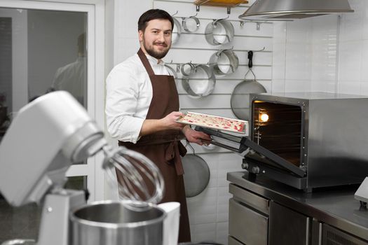 Man pastry chef puts the sponge dough in the oven