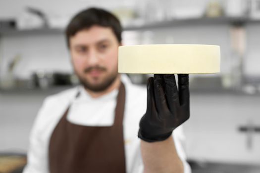 Male pastry chef holds a frozen mousse cake and prepares it for the icing.