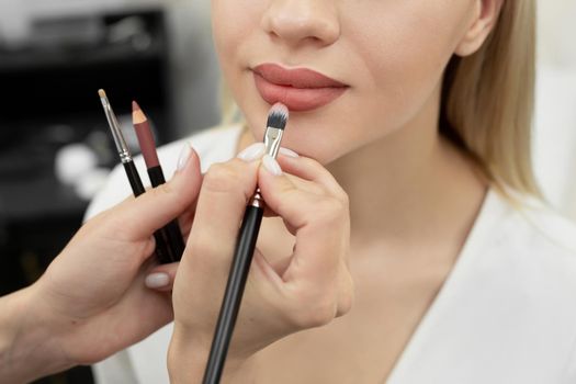 Make-up artist cosmetologist paints her lips before a permanent makeup procedure.