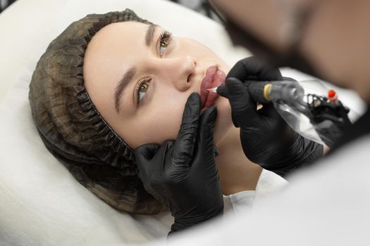 Close-up of the permanent makeup procedure. Lip makeup in the cosmetologist's salon.