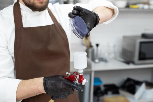 Male pastry chef pours colored chocolate into an airbrush, spray gun