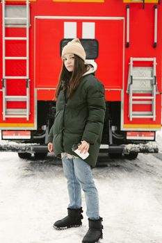 Young beautiful woman drinks coffee in winter on a city street with a red fire truck on the background.