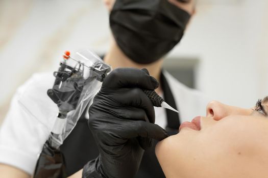 Cosmetologist applies permanent makeup to the lips in the salon.