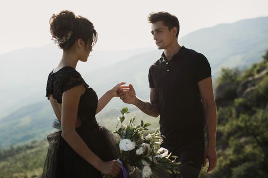 Woman and man in black clothes outdoors. Black wedding dress.