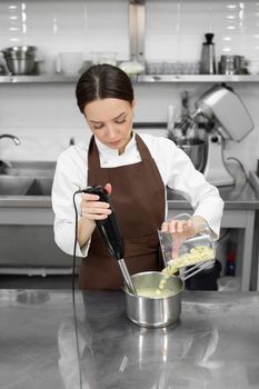 Female pastry chef whips up a mirror icing with white chocolate for a cake with a blender.