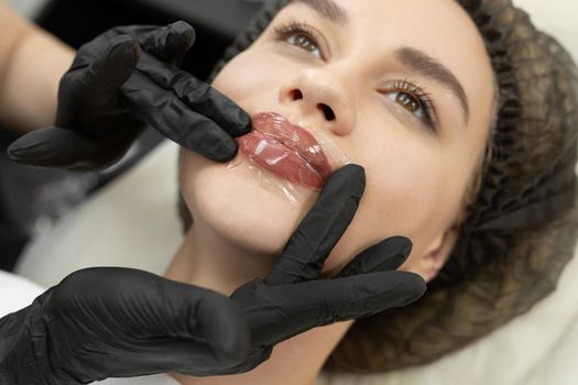 Cosmetologist applies an analgesic cream to the lips and covers it with a transparent film, stretch.