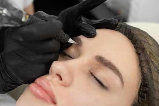 Concept of microblading eyebrows. The cosmetologist performs the procedure of permanent makeup of the eyebrows in close-up.