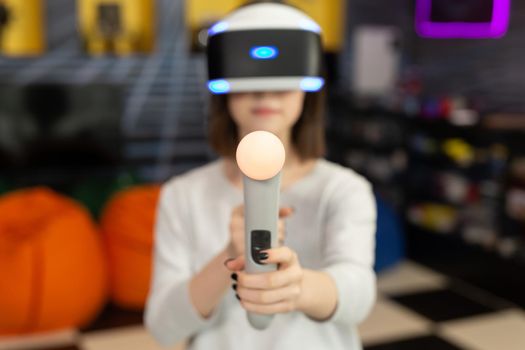 Child, a teenage girl playing on a game console in virtual reality glasses shooting a game with a remote control gun in a game club. VR