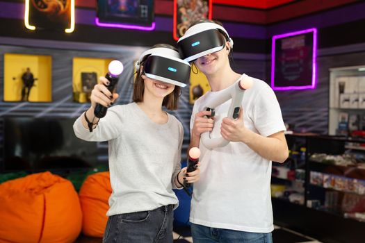 Portrait of teenagers, a boy and a girl with a virtual reality headset in glasses and hand movement controllers in a game club.