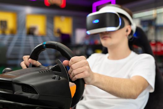 Teenage boy wearing virtual reality glasses, who holds on to the steering wheel and plays a computer game on the console