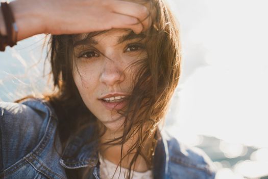 Beautiful young woman at the ocean standing against a turquoise blue sea with her hair blowing in the breeze