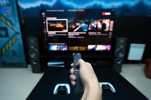 Close-up of a hand with a remote control from the console, choosing a computer game on a large TV.