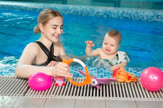 Young mother and her baby daughter play in the pool.