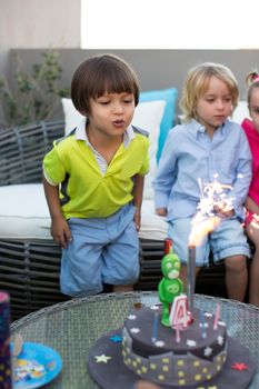 Kids birthday party. Child blowing out candles on colorful cake.