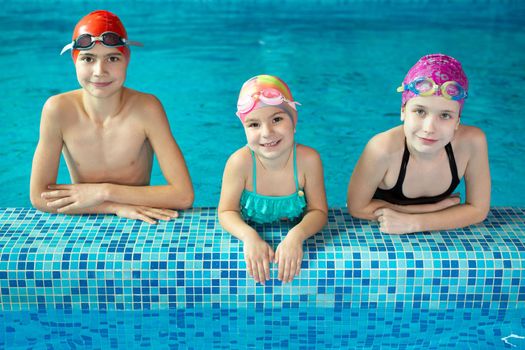 A group of joyful schoolchildren smiling looking at the camera at the edge of the pool during practice