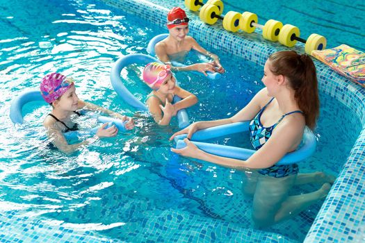 Young female instructor teaches children to swim in the pool.