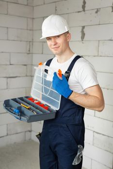Handsome male construction worker with a tool box isolated against a brick wall.