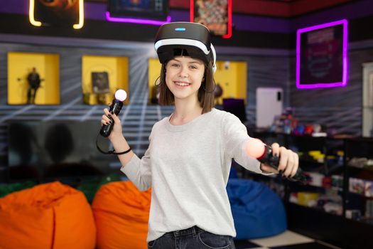 Child, a teenage girl playing on a game console in virtual reality glasses shooting a game with a remote control gun in a game club. VR