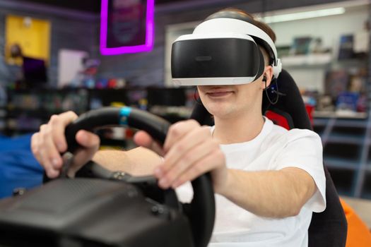 Teenage boy wearing virtual reality glasses, who holds on to the steering wheel and plays a computer game on the console