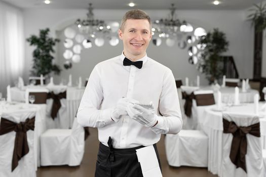 Waiter in a white shirt and bow tie writing down an order in a cafe.