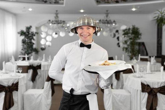 Male waiter with a tray lid on his head in a restaurant.