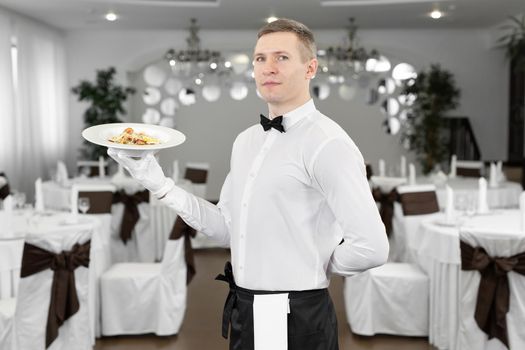 Young happy waiter while serving food in a restaurant.