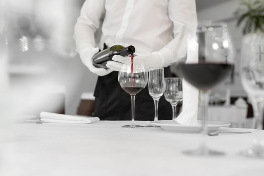 Male waiter in white gloves pours red wine into a glass.