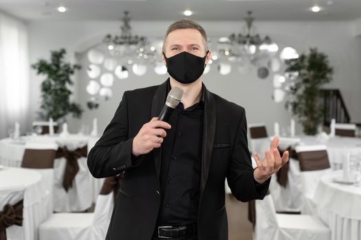 Showman in a suit and protective mask with a microphone in his hands in the banquet hall of rastoran.