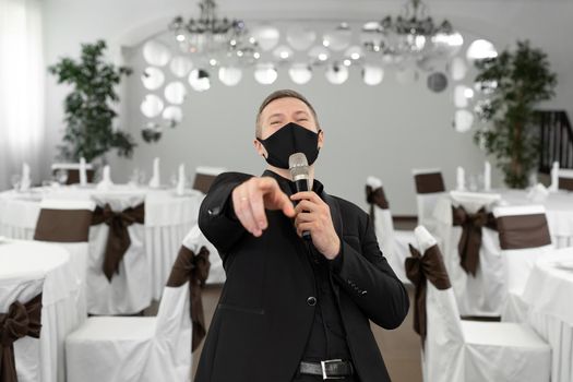 Showman in a suit and protective mask with a microphone in his hands in the banquet hall of rastoran.