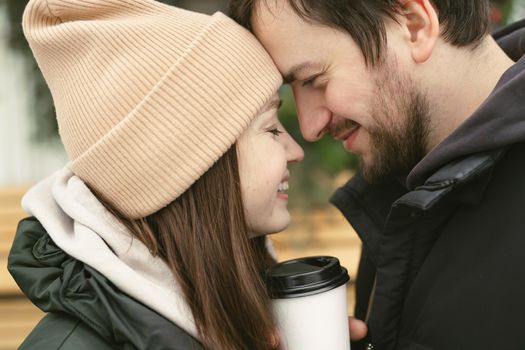Loving beautiful couple on a winter day. A man hugging his happy woman, drinking hot tea or coffee while walking in the fresh air.