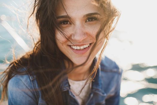 Beautiful young woman at the ocean standing against a turquoise blue sea with her hair blowing in the breeze