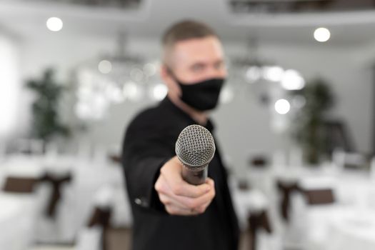 Showman in a suit and protective mask with a microphone in his hands in the banquet hall of rastoran.