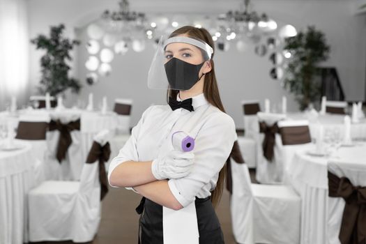 Woman wearing a face mask and holding an infrared thermometer on her forehead to check the body temperature for symptoms of the virus.