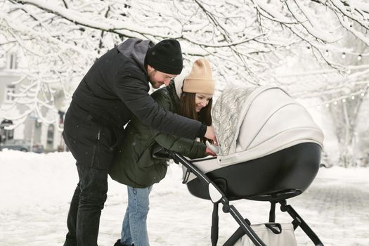 Portrait of a happy young parents stand and kissing with a stroller baby in a winter park