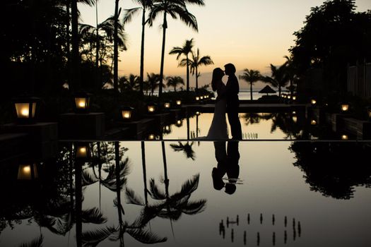 Silhouettes of the bride and groom at sunset. The reflection in the pool