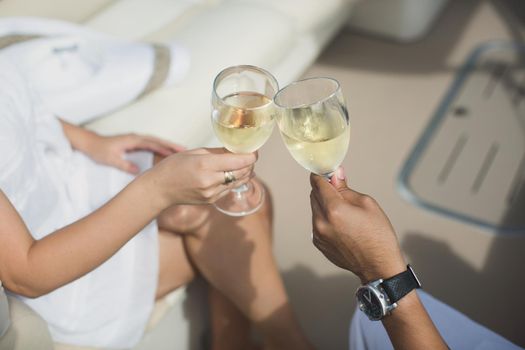 Lovers celebrate their honeymoon on a yacht. Newly married couple clink glasses with champagne