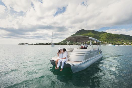 Young couple is sailing on a yacht in the Indian ocean. Man and woman sit on the edge of the yacht