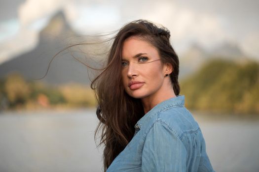 Young girl traveler stands on the beach against the mountain and enjoy the beauty of the sea landscape. Young girl loves wild life, travel, freedom.