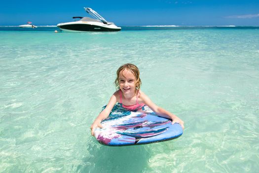 Little baby girl - young surfer with bodyboard has a fun on small ocean waves. Active family lifestyle