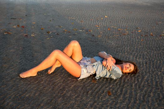 Young girl lying on the sand at sunset