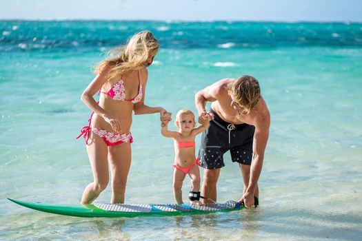 happy family teaching the daughter to stand on the surf in the ocean. concept about family, sport, active people