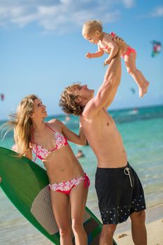 Young and beautiful parents playing with his daughter on the beach