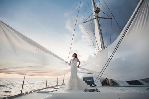 Happy bride on a yacht. White yacht with sail set goes along the island