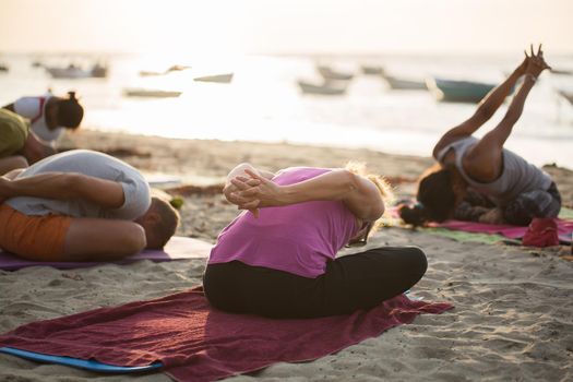 Women doing yoga exercises or supported pigeon pose on an empty beach of the Indian ocean in Mauritius