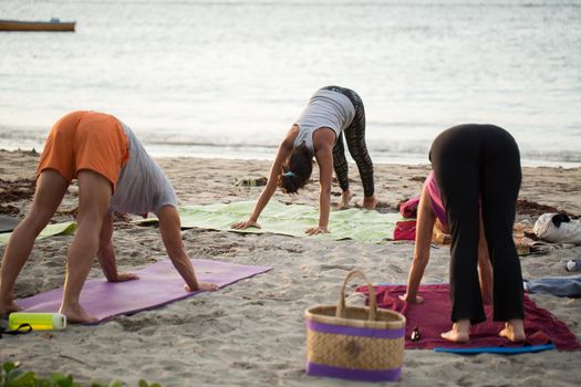 Women doing yoga exercises or supported pigeon pose on an empty beach of the Indian ocean in Mauritius