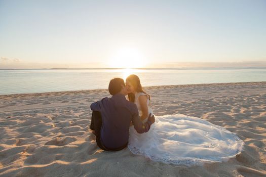 bride and groom sit on the sand